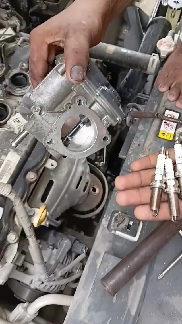 A Mian Autos mechanic holding new spark plugs beside a cleaned throttle body during engine tuning