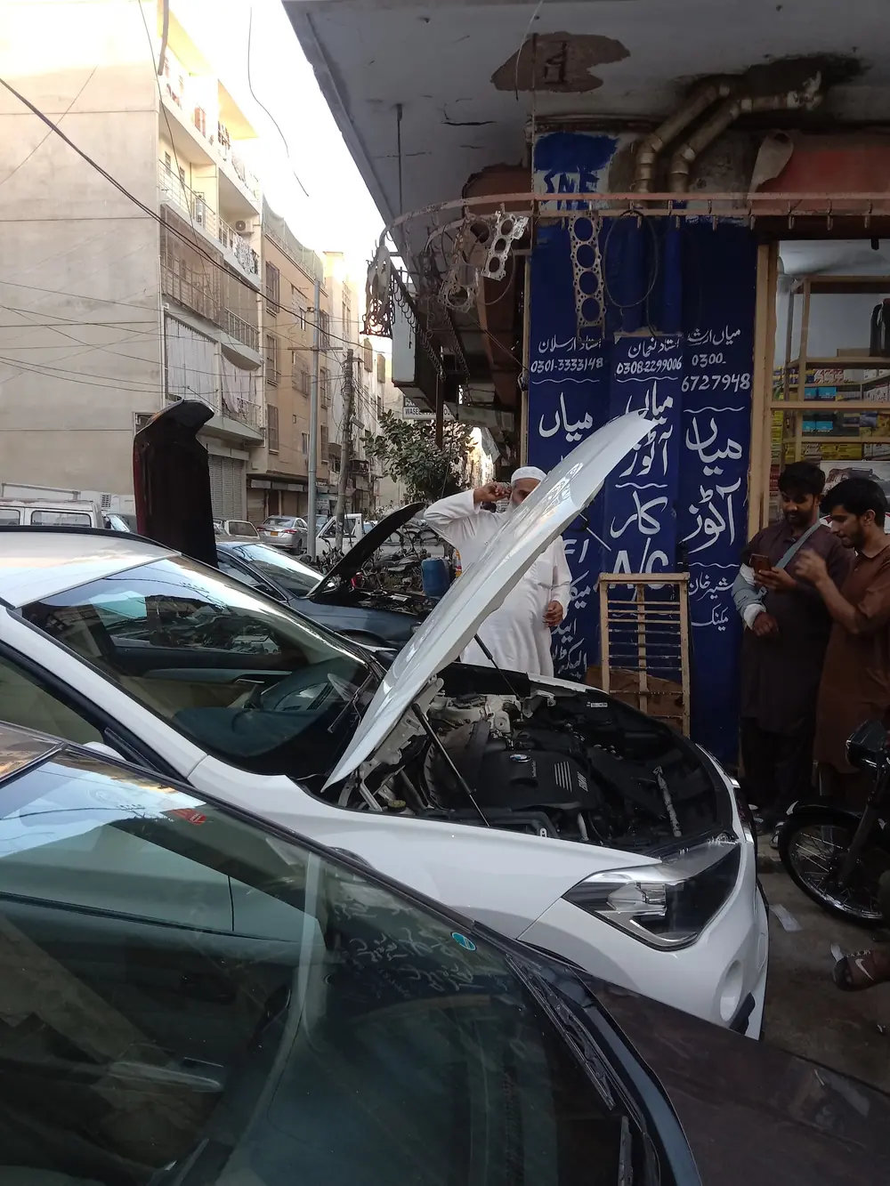 The workshop's blue wall with Mian Autos painted in Urdu, beside a car under repair